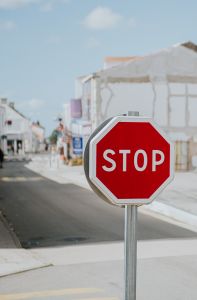 A red stop sign stands prominently in an empty street lined with white buildings under a clear blue sky, signaling caution to pedestrians and vehicles