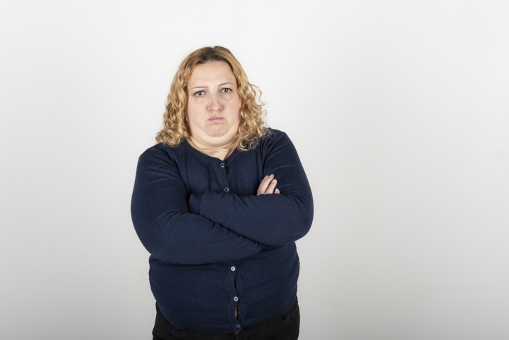 Portrait of plus size blonde woman with angry expression and arms crossed looking seriously at camera
