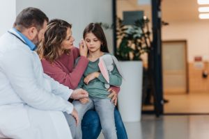 Girl patient at examination in a modern clinic with her mother, sitting in corridor, talking with doctor. Emotional support during medical examination.