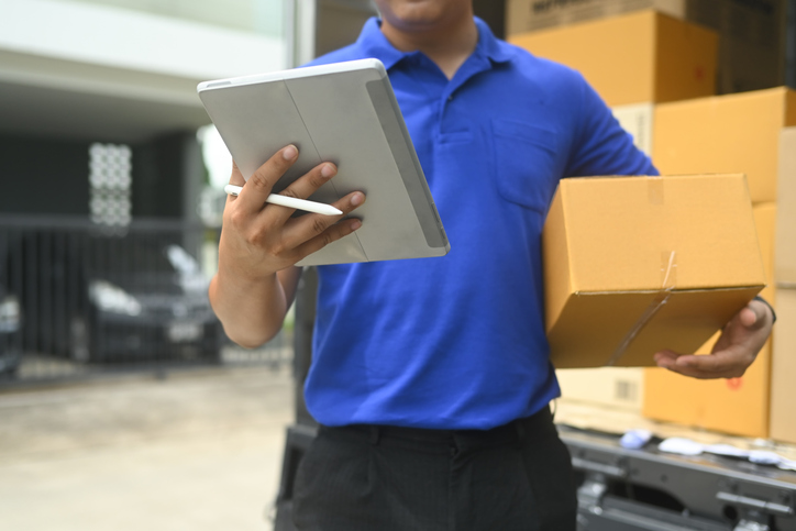 Delivery worker holding a cardboard box and using digital tablet. E-commerce, shipping and delivery services concept