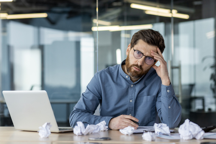 Stressed businessman at office desk with laptop and crumpled papers