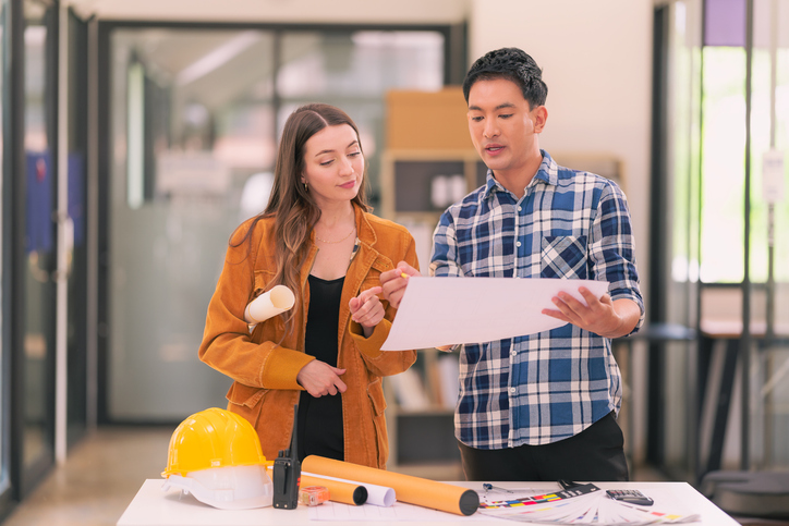 Architects and engineers examining construction project printing sheets. The construction supervisor talks with the project owner about the structural materials in the office.