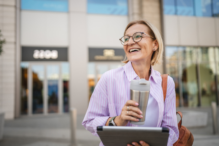 Happy mature woman sit with thermos use digital tablet on the street
