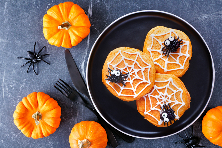 Spooky Halloween spider web pumpkin pancakes with blackberry spiders against a dark stone table