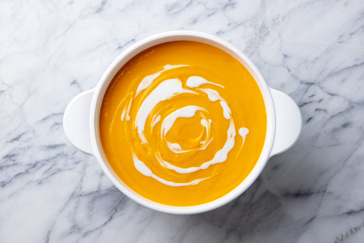 Pumpkin soup in white pot, saucepan, bowl. Grey background. Top view. Close up.