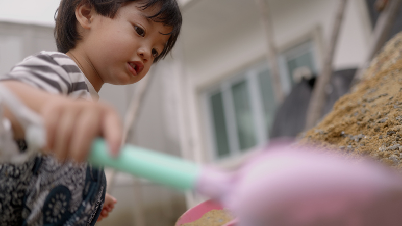 Happy Asian boy enjoy play in the sand pile and mud, scooping up sand and mud to build houses.