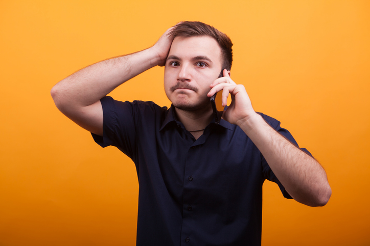Young man with hand on his head while talking on the phone
