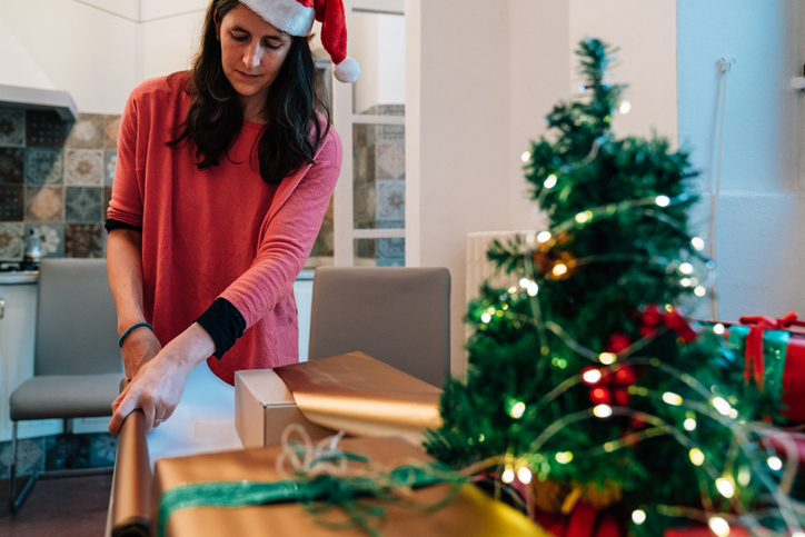 Woman wrapping christmas gifts at home with christmas tree