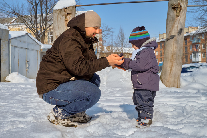 Father and son playing outdoors in the snow on a sunny winter day.