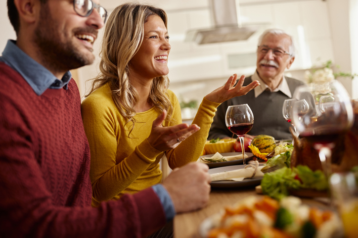 Happy woman having lunch with her husband and senior father at dining table.