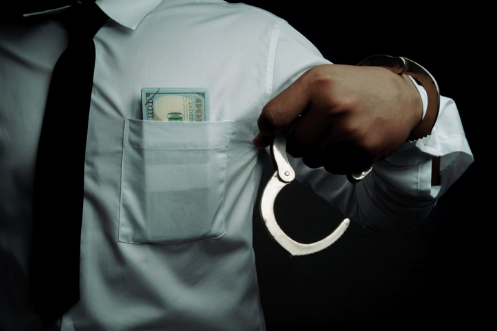 Young businessman standing holding money and handcuffs attached to his arm Concept Corrupt police, bad cop, bribe police.