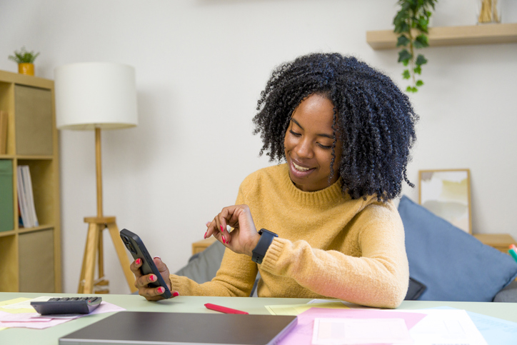 Young accountant managing time efficiently with smartwatch and phone
