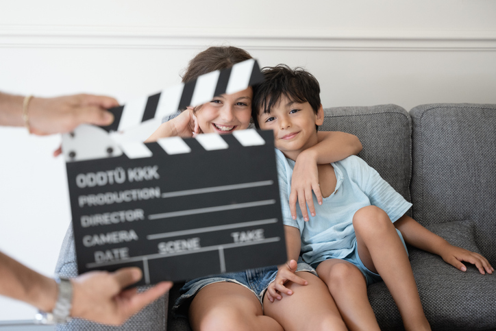 Siblings posing on the couch at home behind a movie clapper board