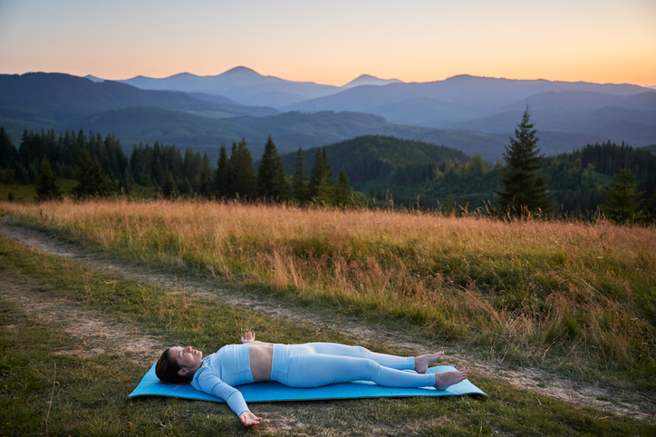 Woman practicing yoga outdoors in the mountains in a serene, natural setting.