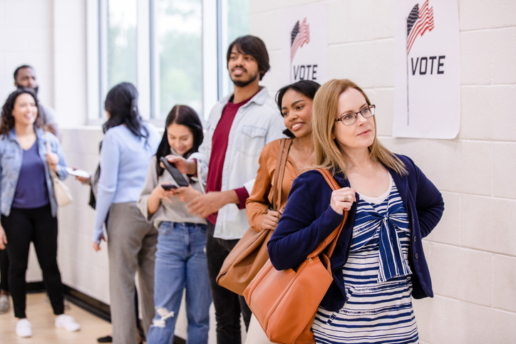 Diverse group of voters stand in line patiently waiting for their turn to sign in