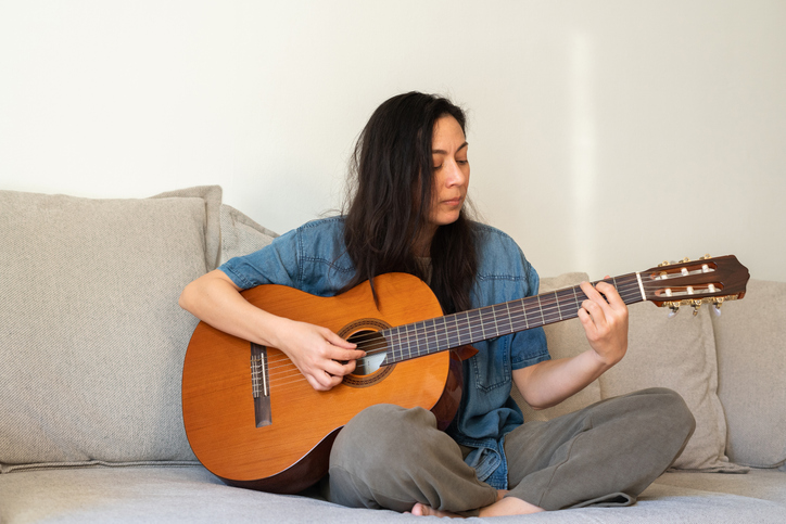 Woman playing acoustic guitar on sofa at home