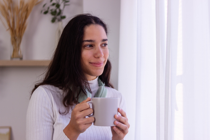 Young woman enjoying a cup of coffee by the window in a cozy home