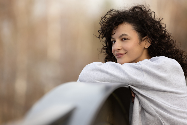 A beautiful girl with dark curly hair is relaxing outdoors, smiling and looking around