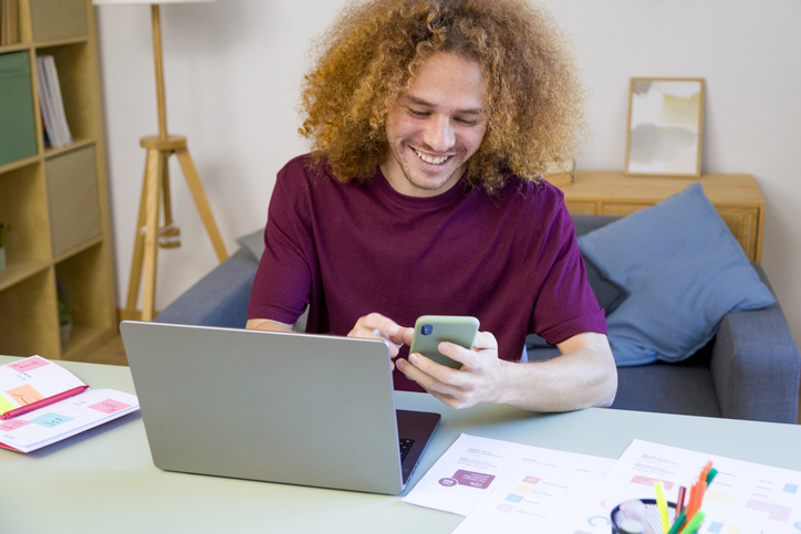 Young man working from home using laptop and smartphone
