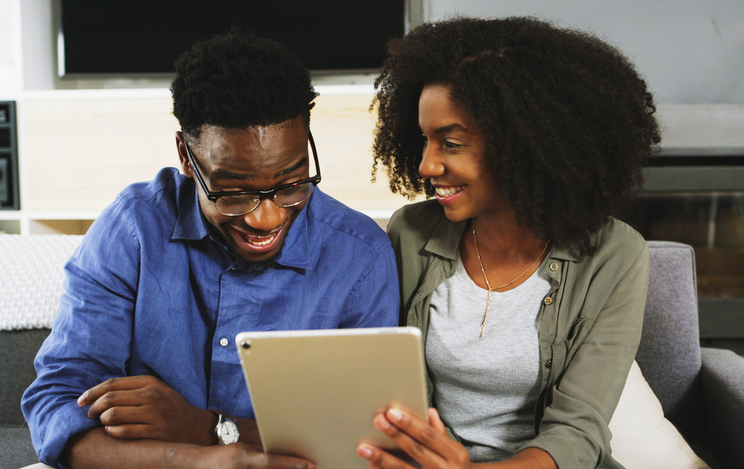Home, couple and smile on tablet on sofa at living room on website for house insurance and security. Apartment, African people and satisfied on internet for offer, deal and options on life policy