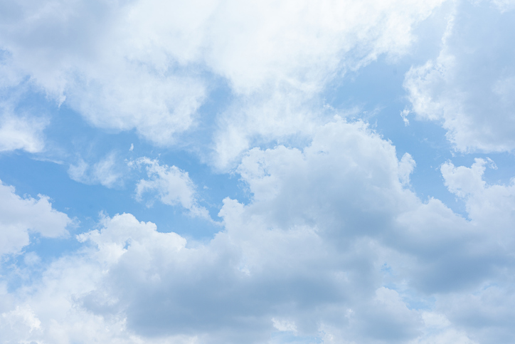 Beautiful fluffy white clouds drift across a bright blue summer sky