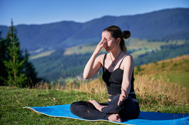 Woman practicing yoga outdoors in the mountains in a serene, natural setting.