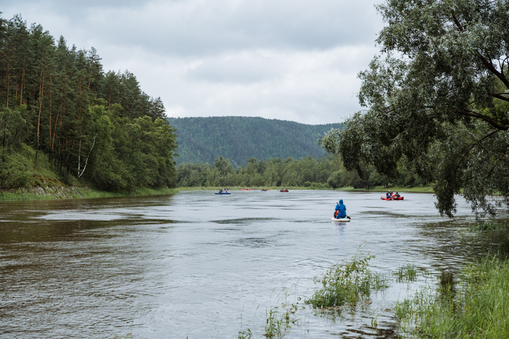 A group of people peacefully kayaking down a calm river, surrounded by nature, under the wide open sky, immersed in the beauty of the picturesque landscape and lush trees