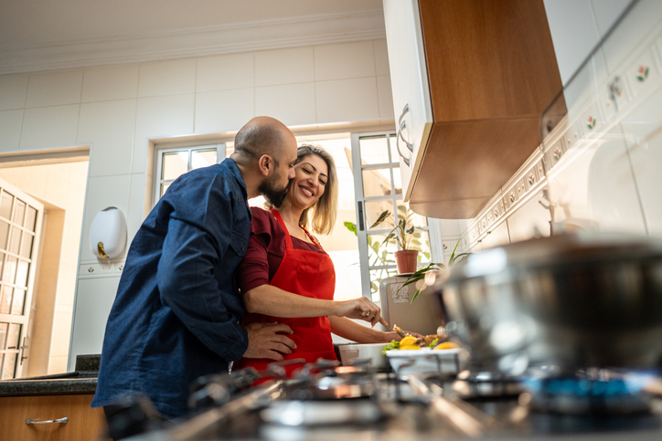 Wife cooking and being kissed by husband on kitchen at home