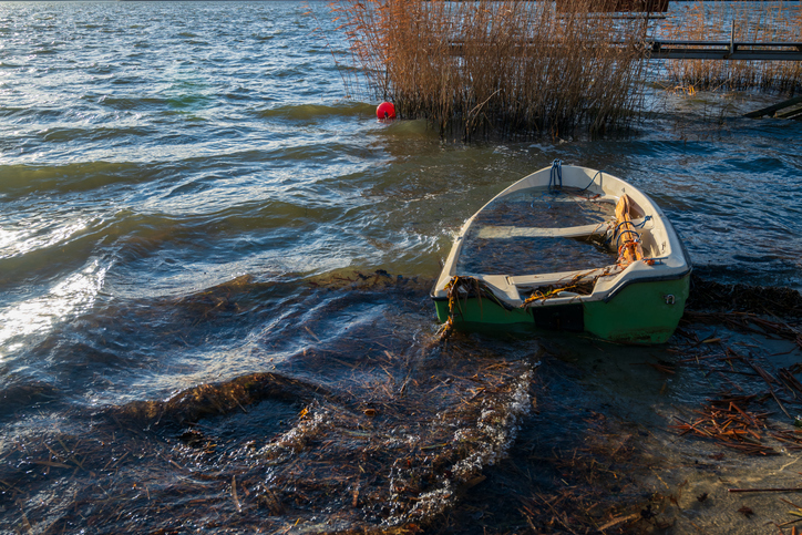 boat abandoned for winter on lake shore full of water inside