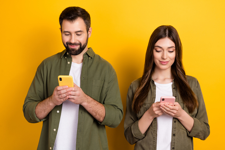 Portrait of attractive focused cheerful couple using device gadget chatting isolated over bright yellow color background