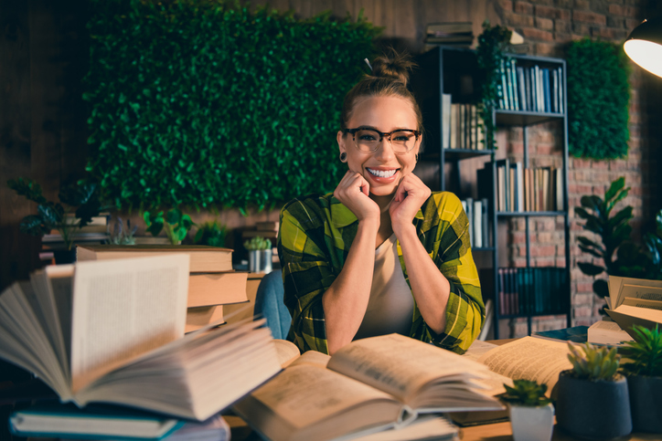 Young woman with glasses enjoying study time at home surrounded by books and greenery