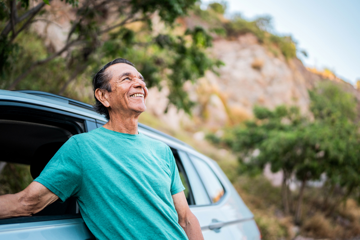 Senior man enjoying the view next to car on mountains background during road trip