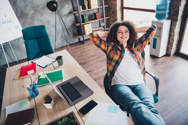 Young businesswoman relaxing in casual office environment with brown curly hair and a checkered shirt