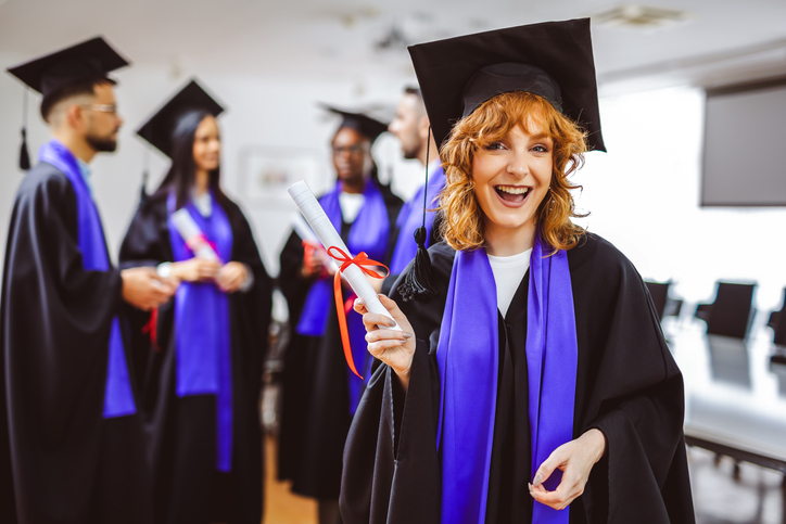 Portrait of gigner graduate student in toga holding her diploma in front of her friends.