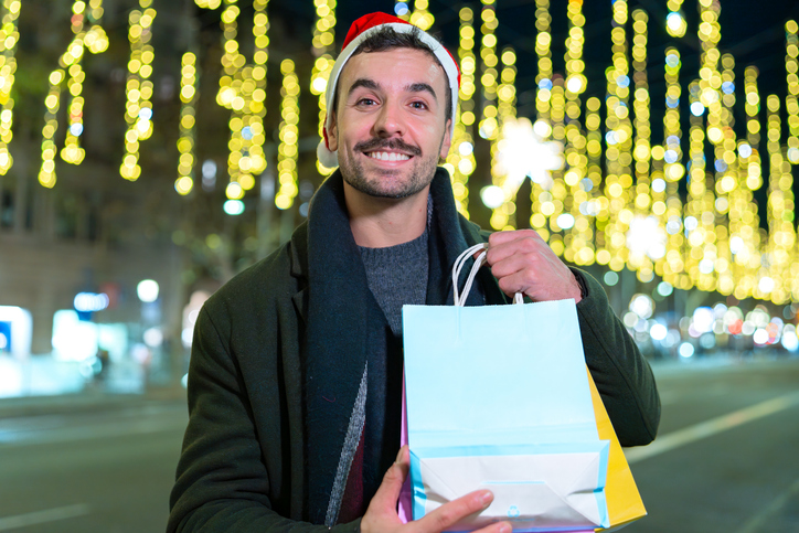 Smiling man in Santa Hat Holding Christmas Shopping Bags