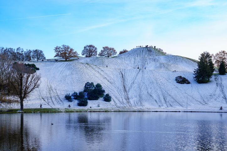 Lake and snow-covered hill in Munich's city park. Sled tracks. Winter fun