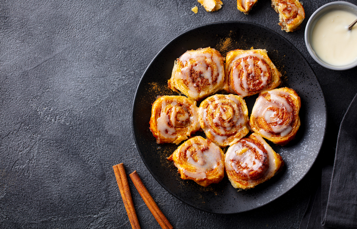 Cinnamon rolls, buns, cinnabons on black plate. Dark background. Close up. Copy space.