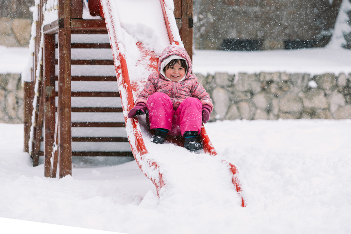 Happy little girl playing in the snow, going down a slide, on a winter day. Precipitation, storm, Filomena, cold, ice, snow, play, enjoy with family, daughters, sons, father and mother.