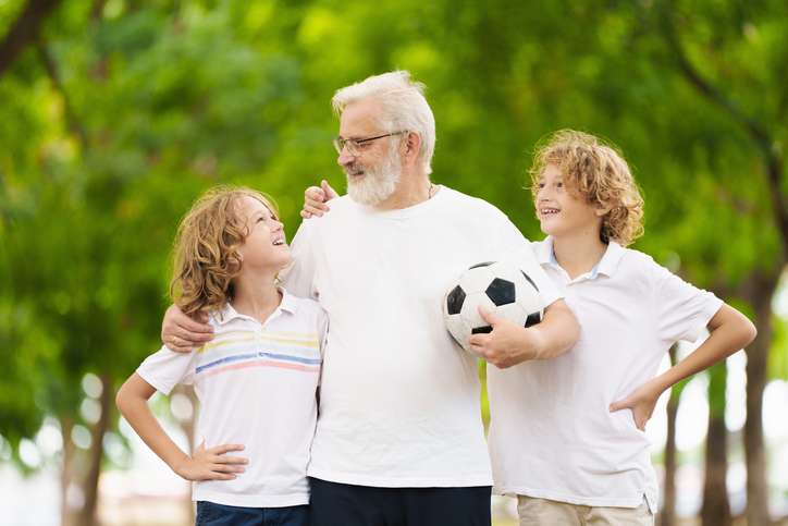 Grandfather and kids play football in summer park