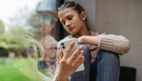 Teenage girl crying after reading cruel text, looking sadly at mobile screen. Teen depression.