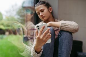 Teenage girl crying after reading cruel text, looking sadly at mobile screen. Teen depression.