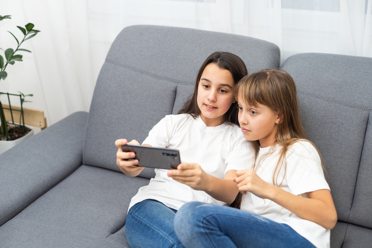 Child with smartphone at home. Two kids using smart phone, surfing internet or using social media. Two kids using online mobile phone, call, watching content, playing video games, sitting on couch