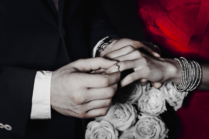 Cropped close up portrait of trendy rich gentleman mr in suit putting on engagement ring accessories on finger to lady mrs having white roses hands, lovely romantic couple isolated on grey background