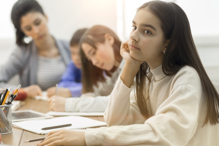 Upset school girl thinking, sitting at boring lesson