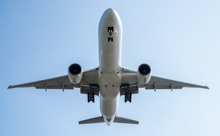 A commercial airplane flying overhead with detailed wings and powerful engines, soaring against a clear blue sky, symbolizing modern aviation, global travel, and the engineering of air transportation.