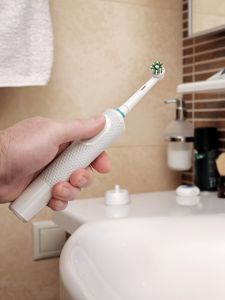 A man holds a modern electric toothbrush against bathroom sink.