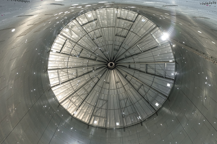 Indoors view of silo grain bin with conical roof. Light from holes. View from bottom to top.