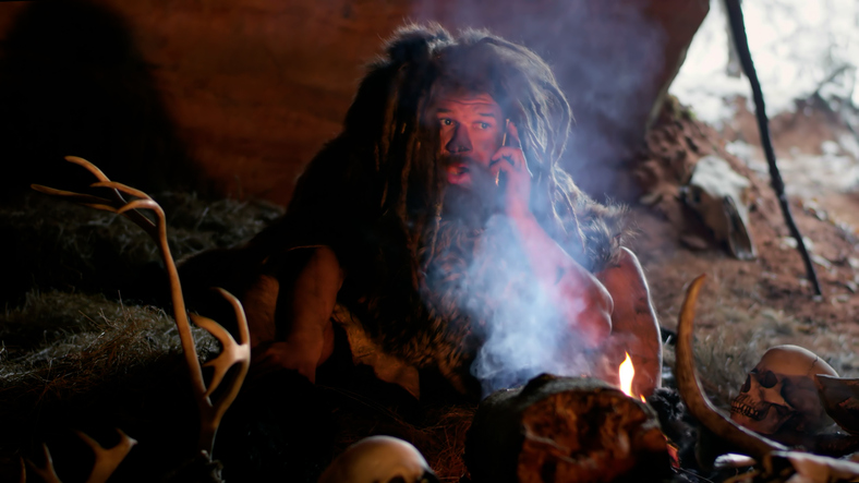 Prehistoric caveman using smartphone in cave