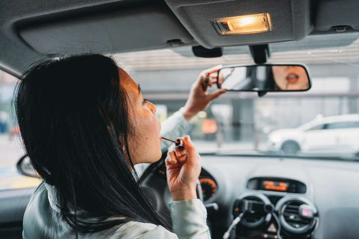 Young woman applying lipstick while driving her car