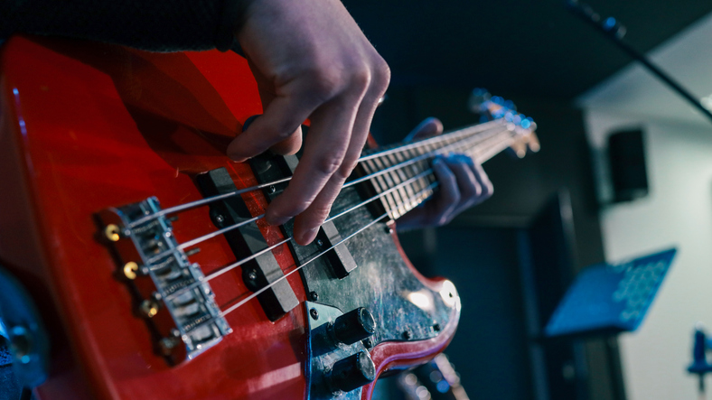 Detail of a musician playing a black electric guitar.